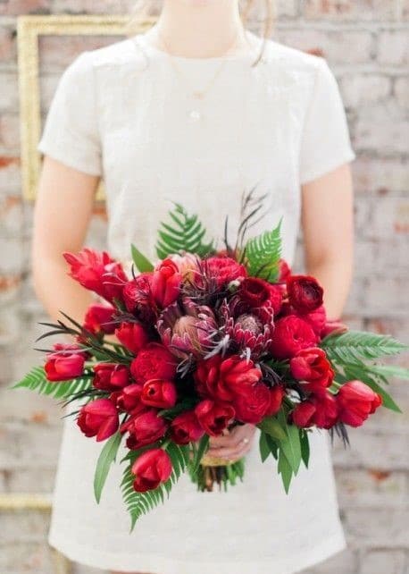 robe de mariée blanche courte avec des manches courtes et un bouquet de tulipes rouges et un feuillage