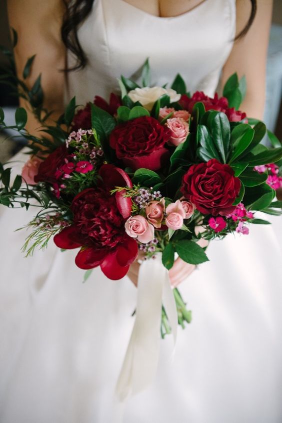Mariée dans une robe blanche bustier avec un bouquet de roses rouge et de fleurs rouges