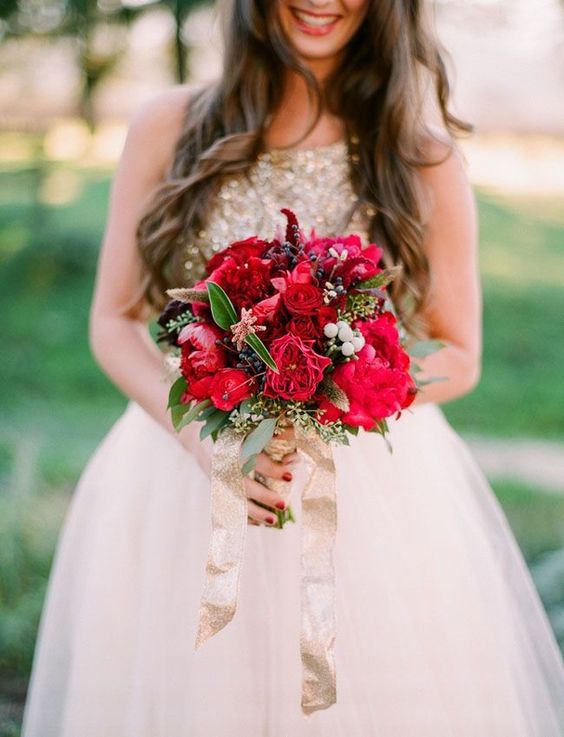 robe de mariée beige, dorée et un bouquet de lys rouges et de roses rouge, un feuillage et un ruban doré