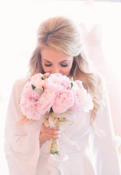 mariée en peignoir blanc et un bouquet de pivoines roses et un feuillage
