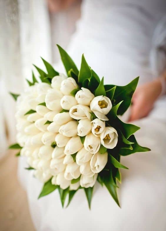 Mariée dans une robe blanche avec un bouquet de tulipes blanches et du feuillage 