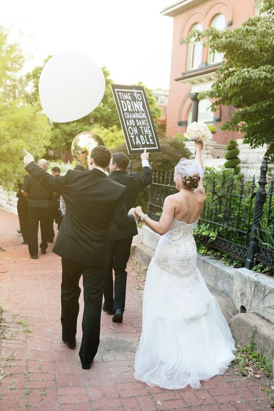 Cortège des mariés et leurs invités dans la rue avec un ballon et une pancarte