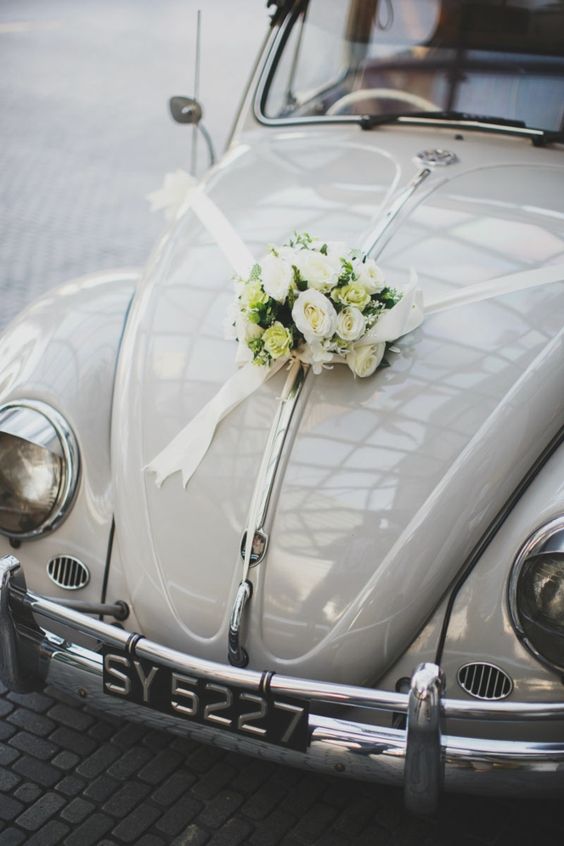 Décoration d'une voiture des mariés avec du ruban et des fleurs blanches, jaunes et du feuillage