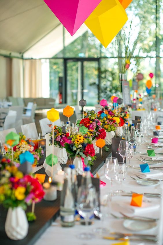 Décoration de table de mariage avec des formes géométriques de couleur et des fleurs multicolores déposées sur une planche en bois