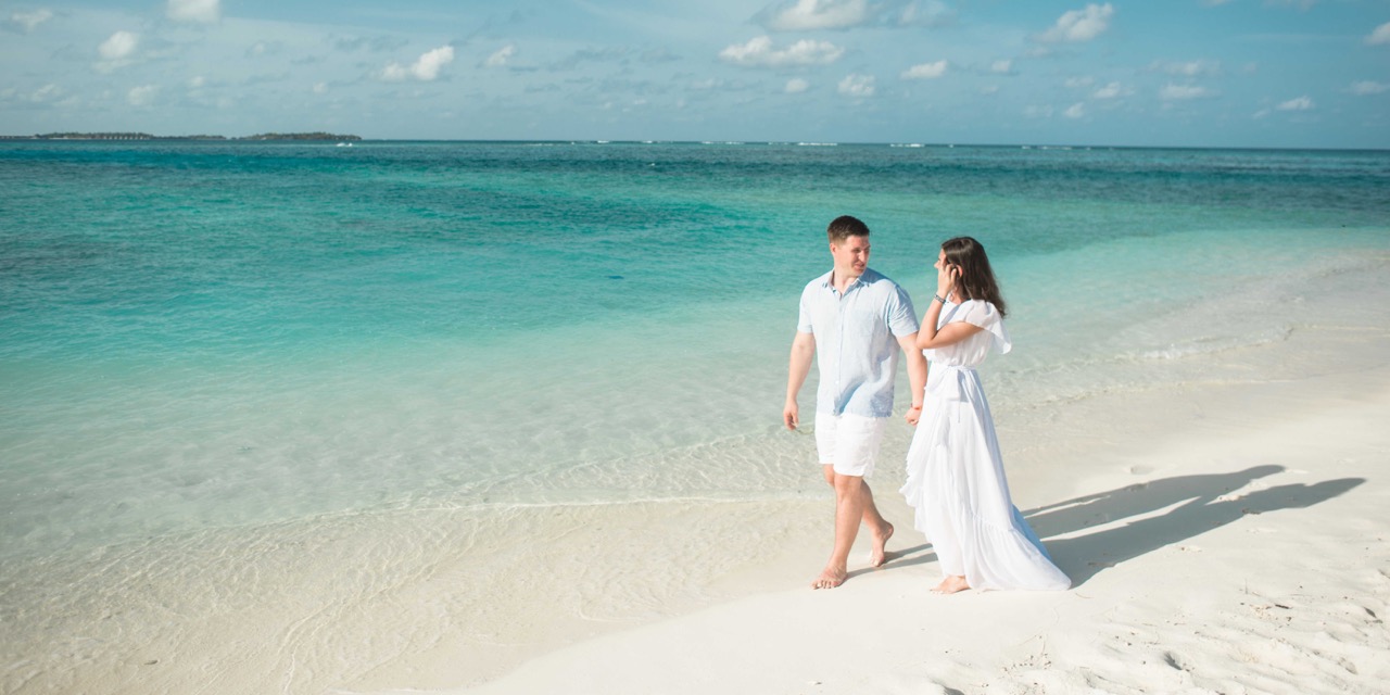 Couple de jeunes mariés se baladant sur une plage de sable blanc lors d'un moment intimiste de sa lune de miel