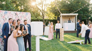 Invités de mariage riant au photomaton, jouant au cornhole et Jenga géant en plein air sous le soleil.